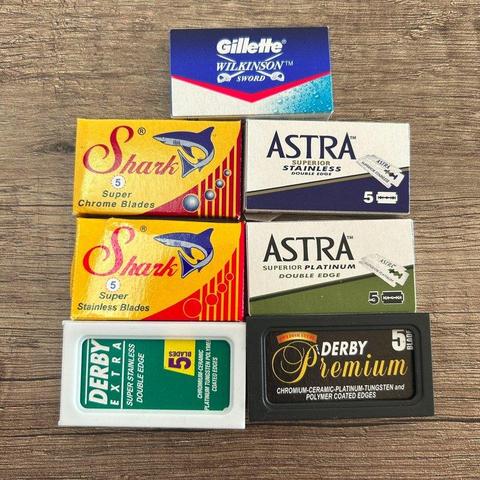 Das Bild zeigt eine Sammlung von Rasierklingenpackungen verschiedener Marken wie Gillette Wilkinson Sword, Shark, Astra und Derby.