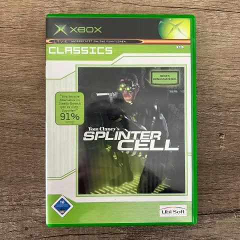 Die Hülle eines Xbox-Spiels mit dem Titel "Tom Clancy's Splinter Cell Classics" mit einem Bild des Hauptcharakters mit Nachtsichtgeräten und einer Waffe. Es gibt auch einen Hinweis auf "Neues Bonusmaterial" und eine Bewertung von 91% von GAMEPRO.