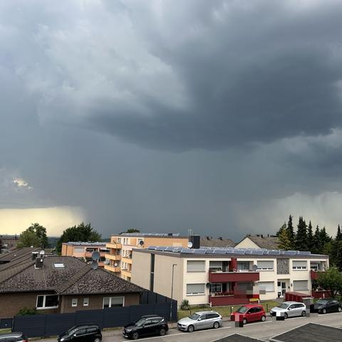 Ein dunkler Wolkenhimmel zieht über einen
 Stadtteil mit Gebäuden und Autos.