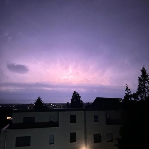 Ein Gewitter bei Nacht mit Blitzen am Himmel über einer Stadt und einigen Gebäuden im Vordergrund.